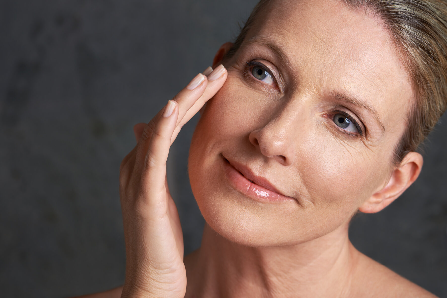 A woman in her fifties touching her cheek, studio light